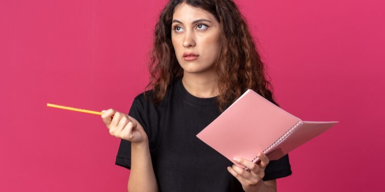 Imagem ilustrativa de mulher com expressão pensativa segurando um caderno e um lápis, representando a dúvida na hora de escrever a palavra