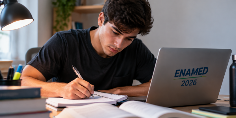 Jovem escrevendo em caderno ao lado de laptop com logo ENAMED 2026 em mesa iluminada.