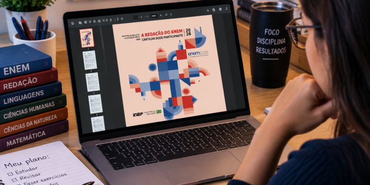 Jovem analisa no notebook a cartilha de redação do Enem 2026 ao lado de livros, caneca motivacional e planejamento de estudos.