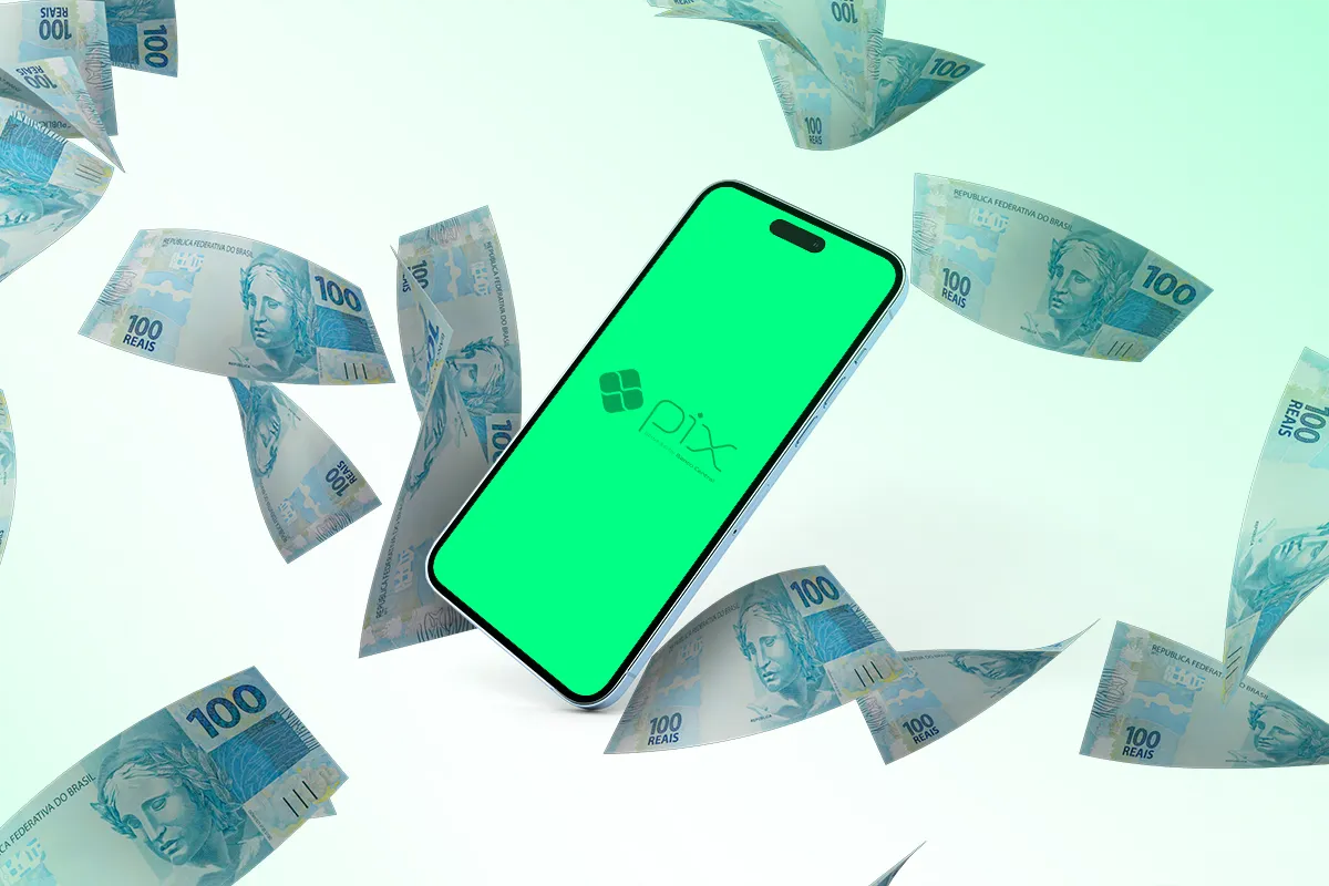 Smartphone com logo Pix em tela verde cercado por notas de 100 reais brasileiras voando.