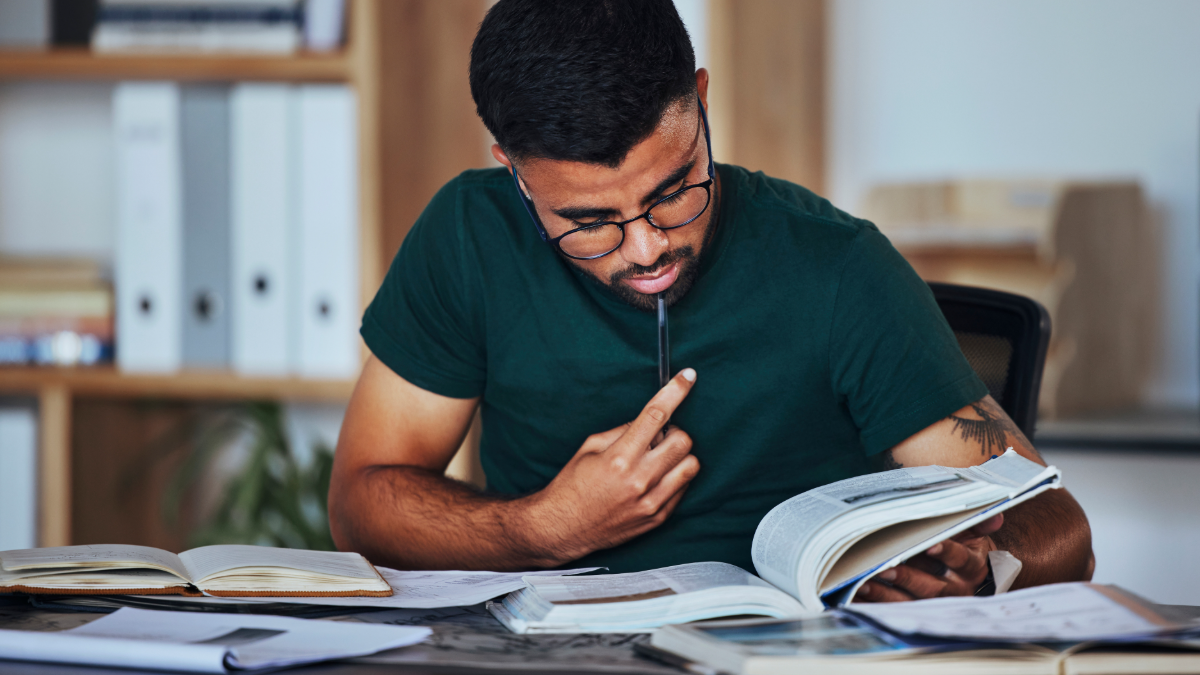 Jovem estudando concentrado cercado por livros em ambiente moderno.