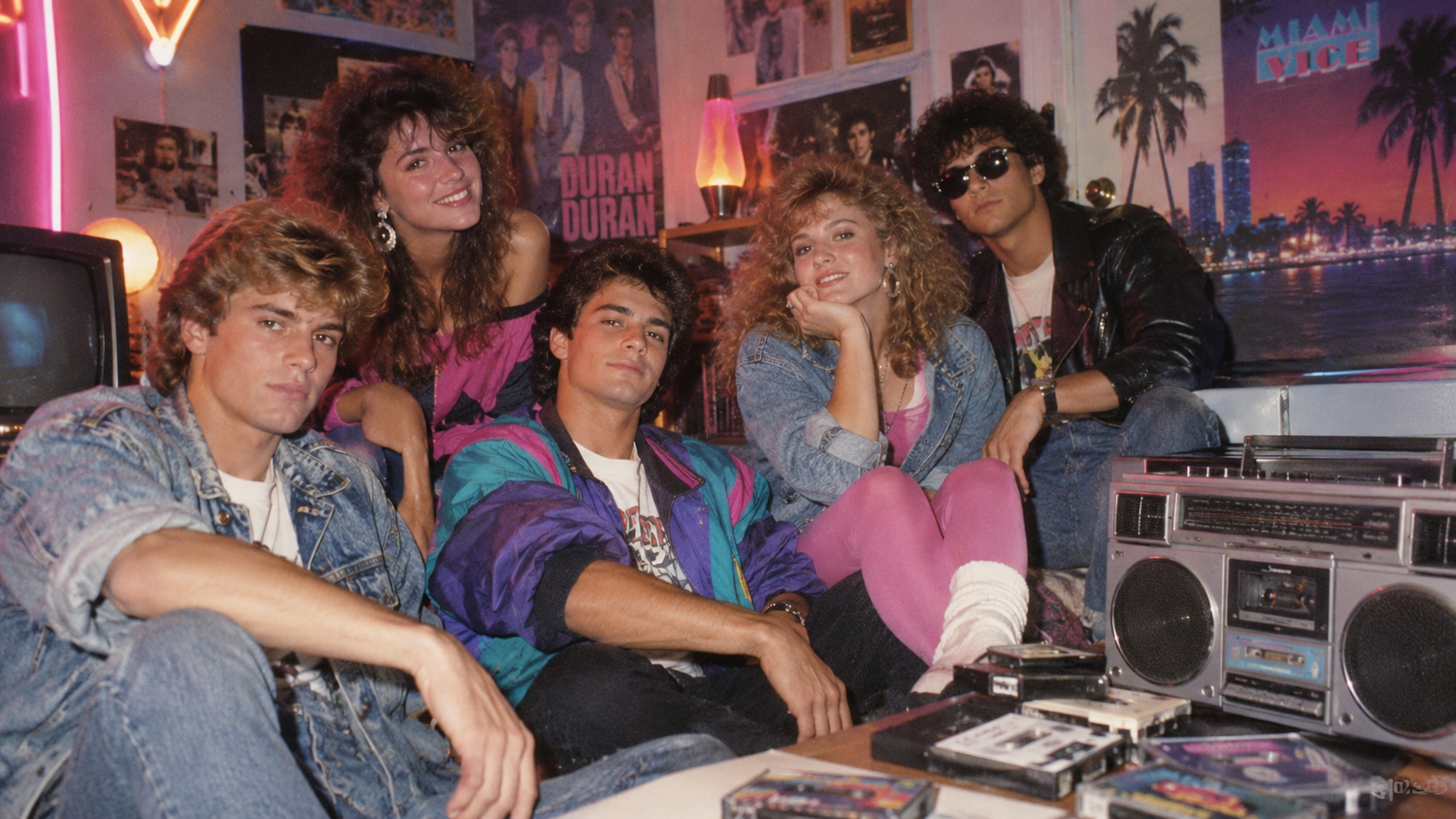 Cinco jovens com roupas dos anos 80, pôsteres de Duran Duran, boombox e fitas cassete sobre mesa.