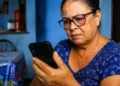 Idosa observa o celular com atenção após alerta do INSS sobre golpe com links falsos.