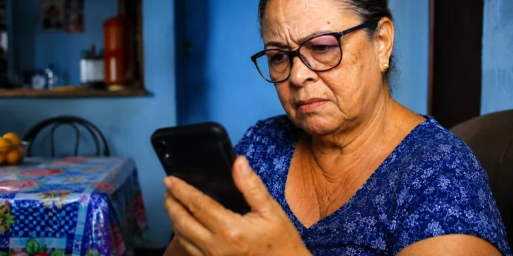 Idosa observa o celular com atenção após alerta do INSS sobre golpe com links falsos.