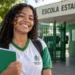 Estudante da rede pública em frente a uma escola estadual representando a ampliação do Pé-de-Meia para todos os alunos em 2027