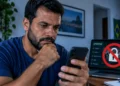 Homem utiliza celular ao lado de notebook com bloqueio de apostas, representando a autoexclusão de plataformas de jogos no Brasil.