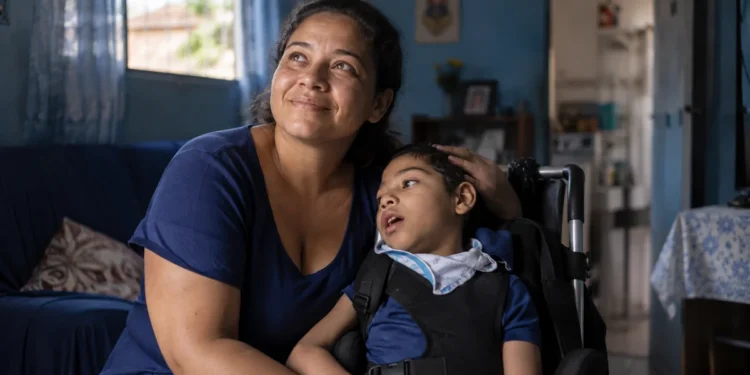 Mãe brasileira cuidando de filho com deficiência em cadeira de rodas, representando o Auxílio Mãe Atípica, com benefício previsto de R$ 600 e adicional de R$ 150 por dependente.
