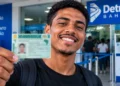 Jovem segura Carteira Nacional de Habilitação em frente ao Detran Bahia, representando as mais de 20 mil vagas do programa de CNH gratuita no estado.