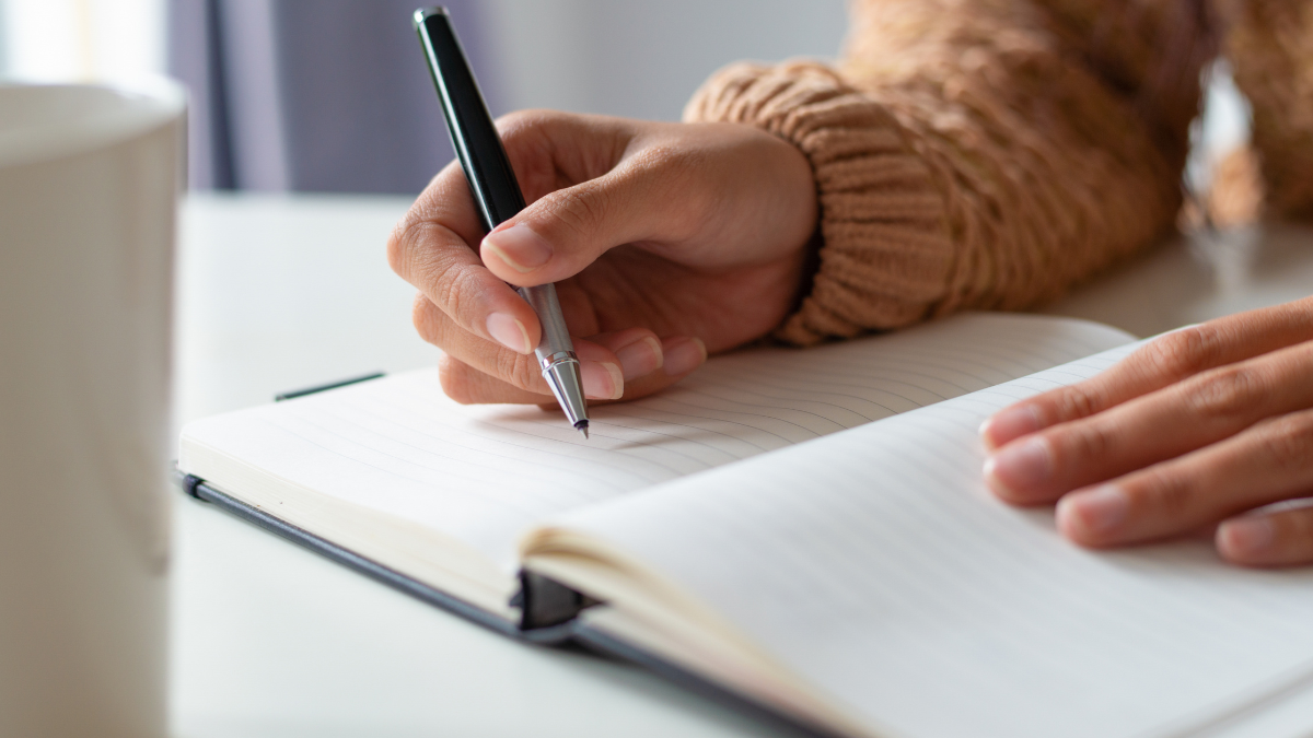 Pessoa estudando para concursos públicos com caderno e caneta.