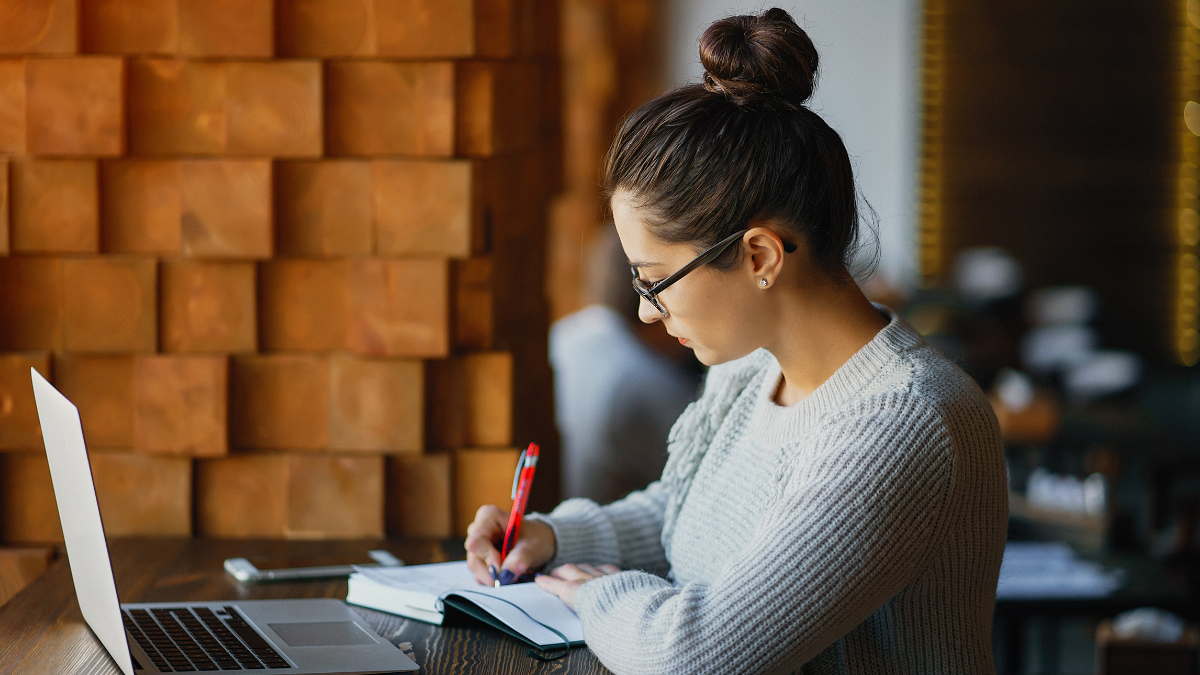 Pessoa estudando com notebook e caderno para preparação para concursos públicos.
