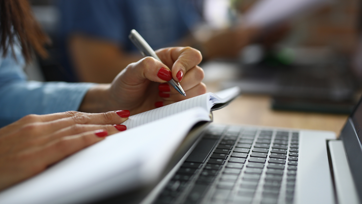 Pessoa estudando para concursos públicos com caderno e notebook em preparação para provas.