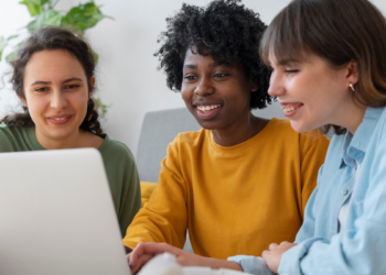 Três pessoas analisam informações sobre concursos públicos em um notebook.