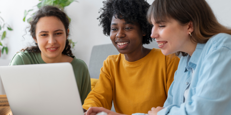 Três pessoas analisam informações sobre concursos públicos em um notebook.