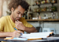 Pessoa estudando para concursos públicos com material de preparação e notebook, representando candidatos em busca de oportunidades no serviço público.