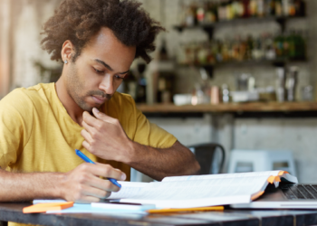 Pessoa estudando para concursos públicos com material de preparação e notebook, representando candidatos em busca de oportunidades no serviço público.