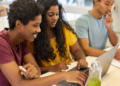 Candidatos estudam para concursos públicos com apoio de notebook e materiais de preparação.