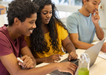 Candidatos estudam para concursos públicos com apoio de notebook e materiais de preparação.