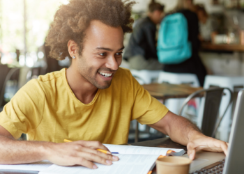 Pessoa estudando para concursos públicos com notebook e materiais de preparação.