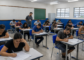 Candidatos realizam prova de concurso público em sala de aula de escola pública.