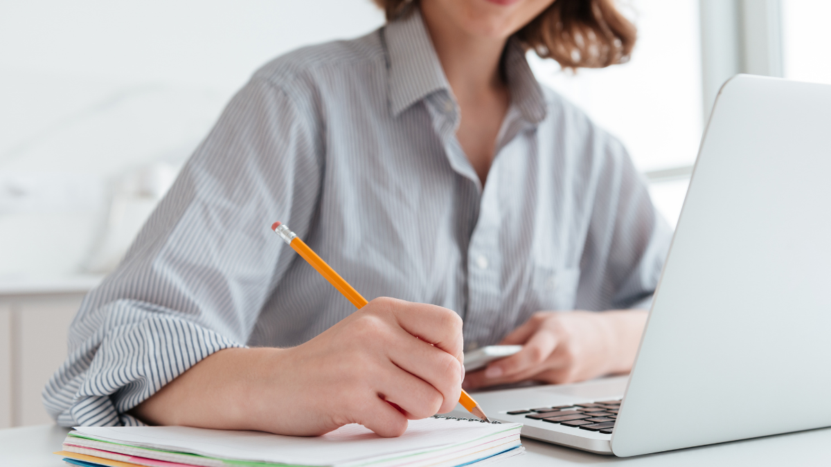 Pessoa estudando para concurso público com caderno e notebook em ambiente de preparação.