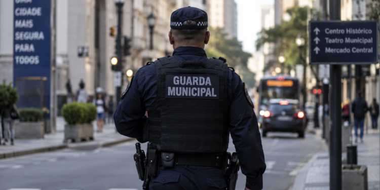 Guarda municipal de costas durante patrulhamento no centro de uma cidade.