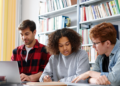 Candidatos estudam juntos para concursos públicos com apoio de notebook e livros.