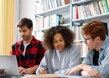 Candidatos estudam juntos para concursos públicos com apoio de notebook e livros.