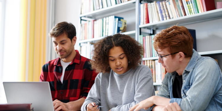 Candidatos estudam juntos para concursos públicos com apoio de notebook e livros.