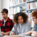 Candidatos estudam juntos para concursos públicos com apoio de notebook e livros.
