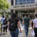 Candidatos a concursos públicos caminham em direção a uma prefeitura com documentos de inscrição.