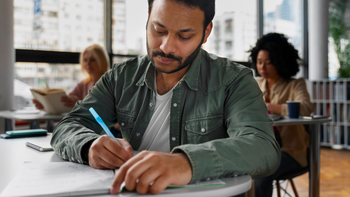 Candidato estudando para concursos públicos com material de preparação sobre uma mesa.