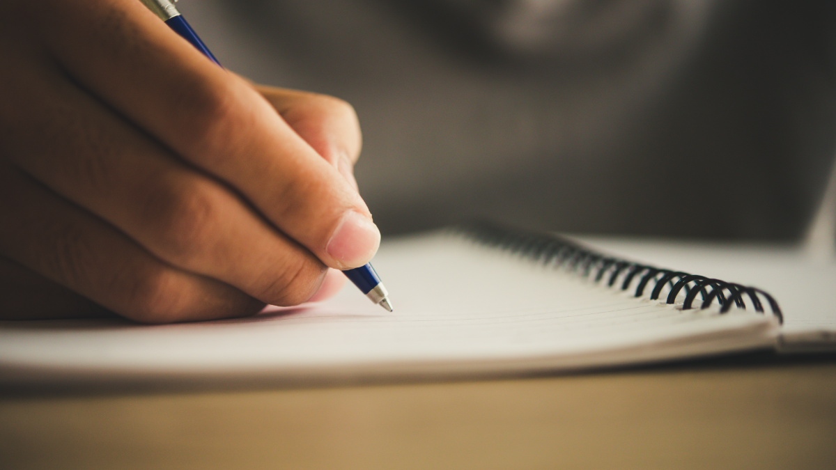 Pessoa escrevendo em caderno durante preparação para concurso público na área de Tecnologia da Informação.