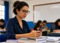 Professora consulta pelo celular informações sobre o cartão de confirmação da PND 2026 em sala de aula.