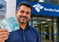 Contribuinte segura notas de reais em frente a uma unidade da Receita Federal, representando a consulta ao lote residual do Imposto de Renda.