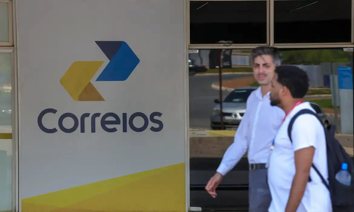 Fachada dos Correios com pessoas em frente a uma unidade da empresa.