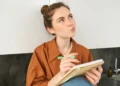 Mulher escreve em caderno enquanto representa dúvida sobre o uso das palavras doze e dose na língua portuguesa.