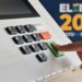 Imagem ilustrativa: dedo pressiona a tecla verde de confirmação do teclado de uma urna eletrônica, ao lado da marca das Eleições 2026