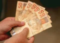 Mãos seguram cédulas de real, representando o pagamento do INSS de até R$ 8.475,55 para beneficiários com cartão final 5 e 0.