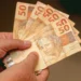 Mãos seguram cédulas de real, representando o pagamento do INSS de até R$ 8.475,55 para beneficiários com cartão final 5 e 0.