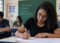 Mulher realiza prova em sala de aula representando a estrutura da Prova Nacional Docente 2026.