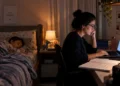 Mãe concurseira estudando no computador enquanto o filho dorme, representando a conciliação entre estudos e maternidade.