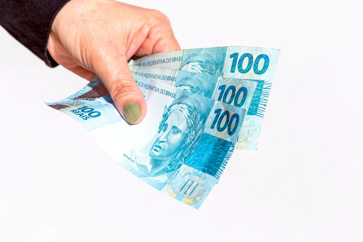 Mão segurando notas de R$ 100, representando o pagamento mensal do Pé-de-Meia Licenciaturas.