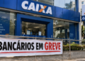 Fachada de agência da Caixa Econômica Federal com faixa indicando greve dos bancários durante paralisação dos funcionários.