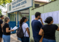 Candidatos consultam listas em frente a uma escola antes da prova do concurso Sedes DF.