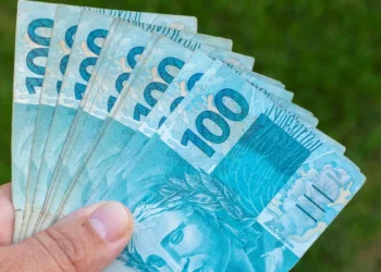 Cédulas de R$ 100 sendo seguradas representam o Saque Calamidade do FGTS de até R$ 6.220 para moradores de cidades recentemente habilitadas.