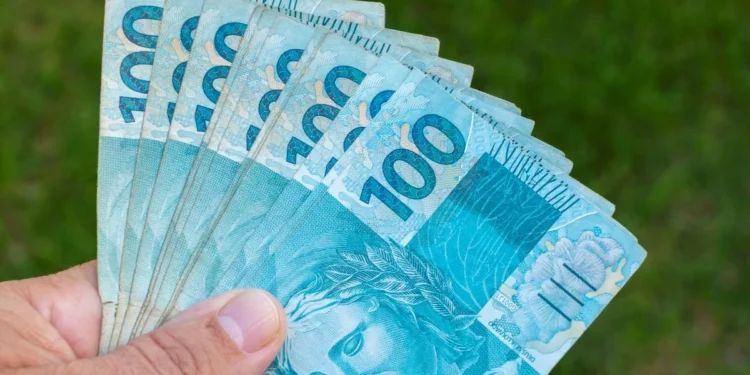 Cédulas de R$ 100 sendo seguradas representam o Saque Calamidade do FGTS de até R$ 6.220 para moradores de cidades recentemente habilitadas.