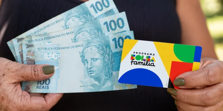 Mãos segurando notas de 100 reais e cartão do Bolsa Família representando o novo valor mínimo de R$ 691