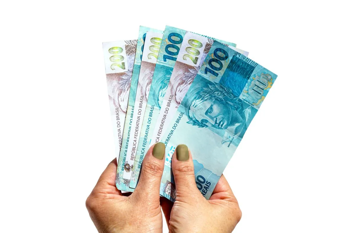 Mãos segurando cédulas de real representando o pagamento do Bolsa Família e acesso aos benefícios sociais durante a greve da Caixa