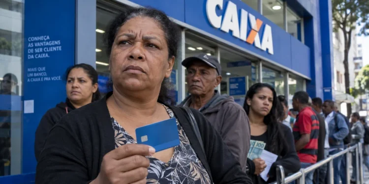 Fila de brasileiros em frente a uma agência da Caixa durante paralisação, com cliente segurando cartão de benefício