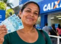 Mulher segura notas de R$ 100 em frente a uma agência da Caixa, representando o pagamento do Bolsa Família de outubro.